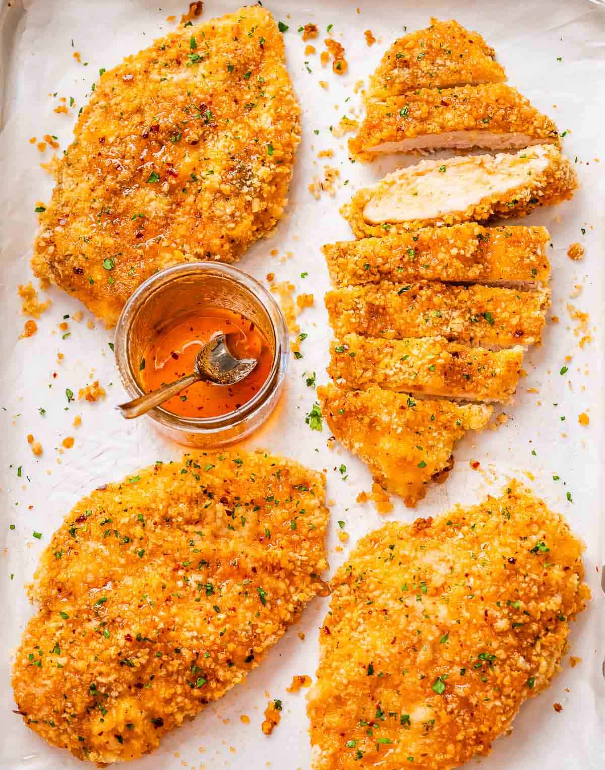 Crispy honey chicken cutlets baked on a tray with a jar of hot honey sauce.