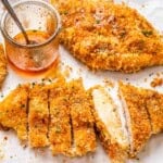 sliced crispy chicken cutlets topped with honey on a sheet pan.