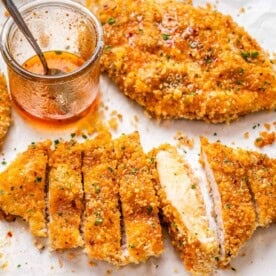 sliced crispy chicken cutlets topped with honey on a sheet pan.