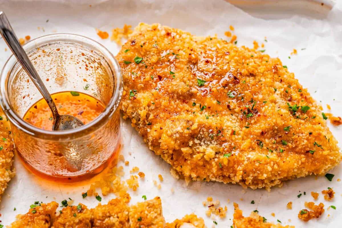 crispy baked chicken bread on a pan with hot honey glaze in a jar.