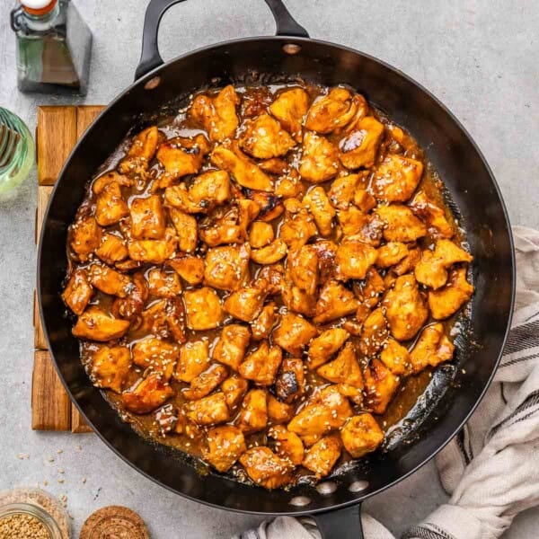a skillet with chicken bites in a hoisin sauce topped with sesame seeds.