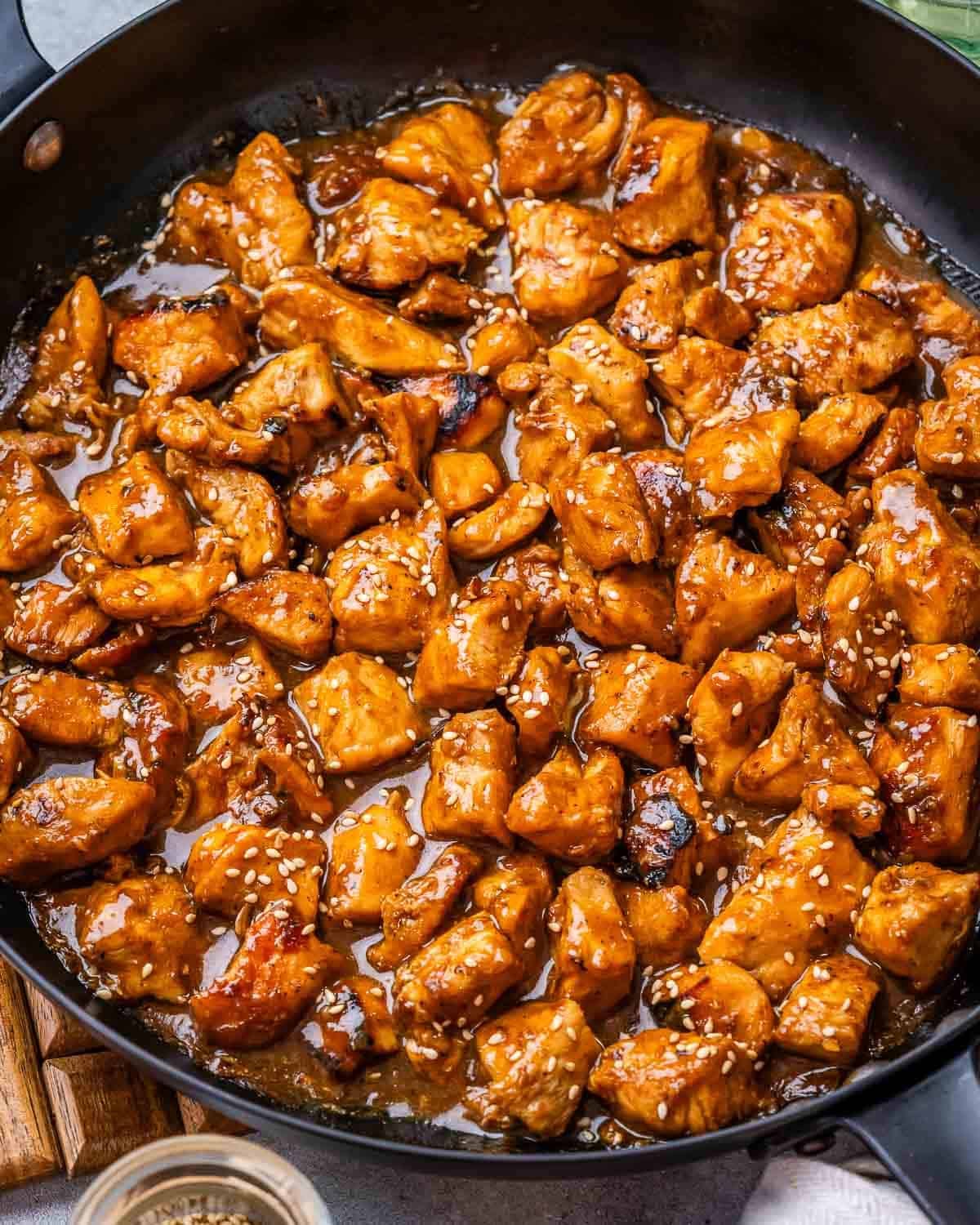 A skillet with hoisin chicken breast chunks garnished with sesame seeds.