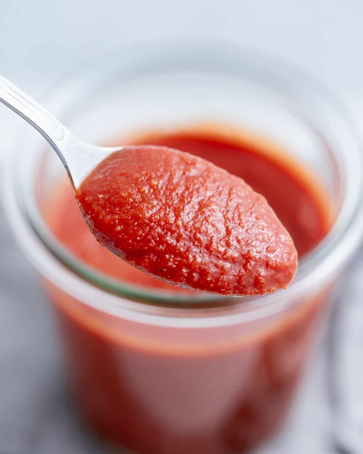 A spoonful of taco sauce above a jar.