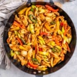 skillet with cooked chicken strips and bell peppers in a sweet sauce topped with sesame seeds.