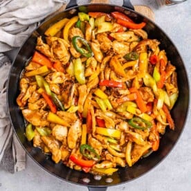 skillet with cooked chicken strips and bell peppers in a sweet sauce topped with sesame seeds.