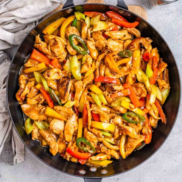 skillet with cooked chicken strips and bell peppers in a sweet sauce topped with sesame seeds.