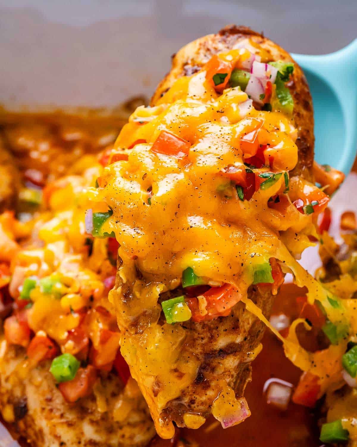 spoon holding up a baked chicken breast topped with salsa and melted cheese.