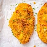crispy baked chicken breast on a sheet pan topped with chopped parsley.