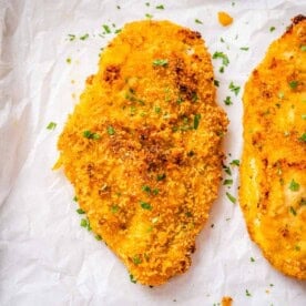 crispy baked chicken breast on a sheet pan topped with chopped parsley.