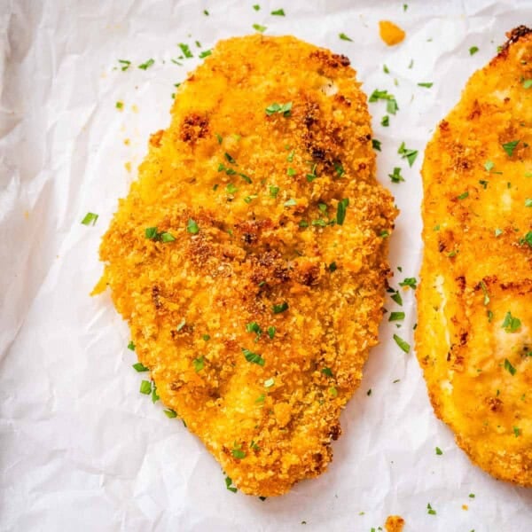 crispy baked chicken breast on a sheet pan topped with chopped parsley.