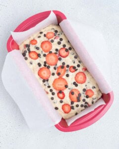 batter added in a baking pan and topped with sliced strawberries and chocolate chips.