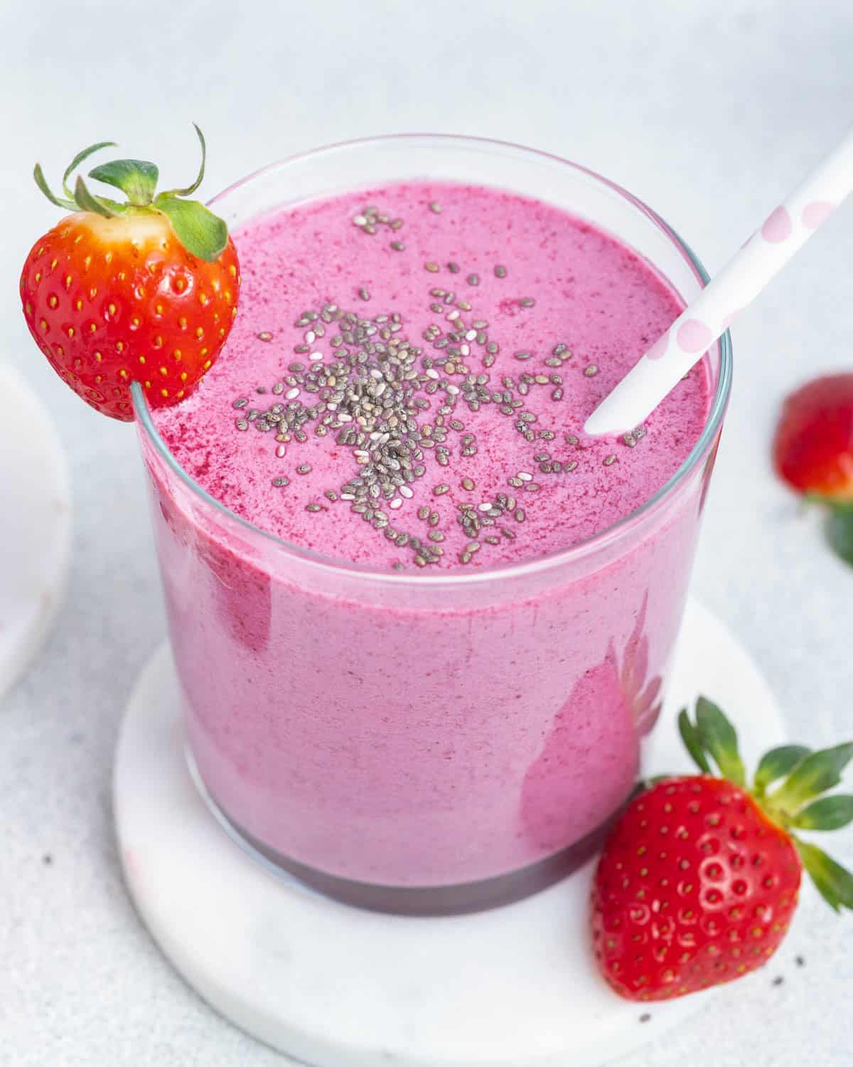 a cup filled with purple looking smoothie, topped with chia seeds and a straw in the cup.