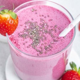 a cup full of smoothie that purple looking, topped with a sprinkle of chia seeds with a straw in the cup.