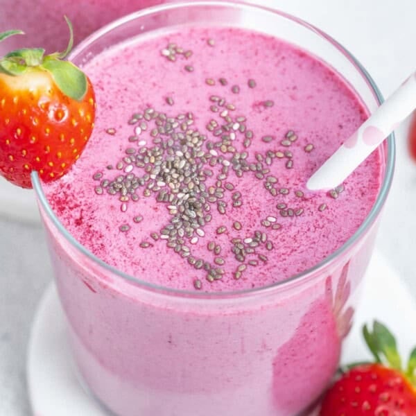 a cup full of smoothie that purple looking, topped with a sprinkle of chia seeds with a straw in the cup.