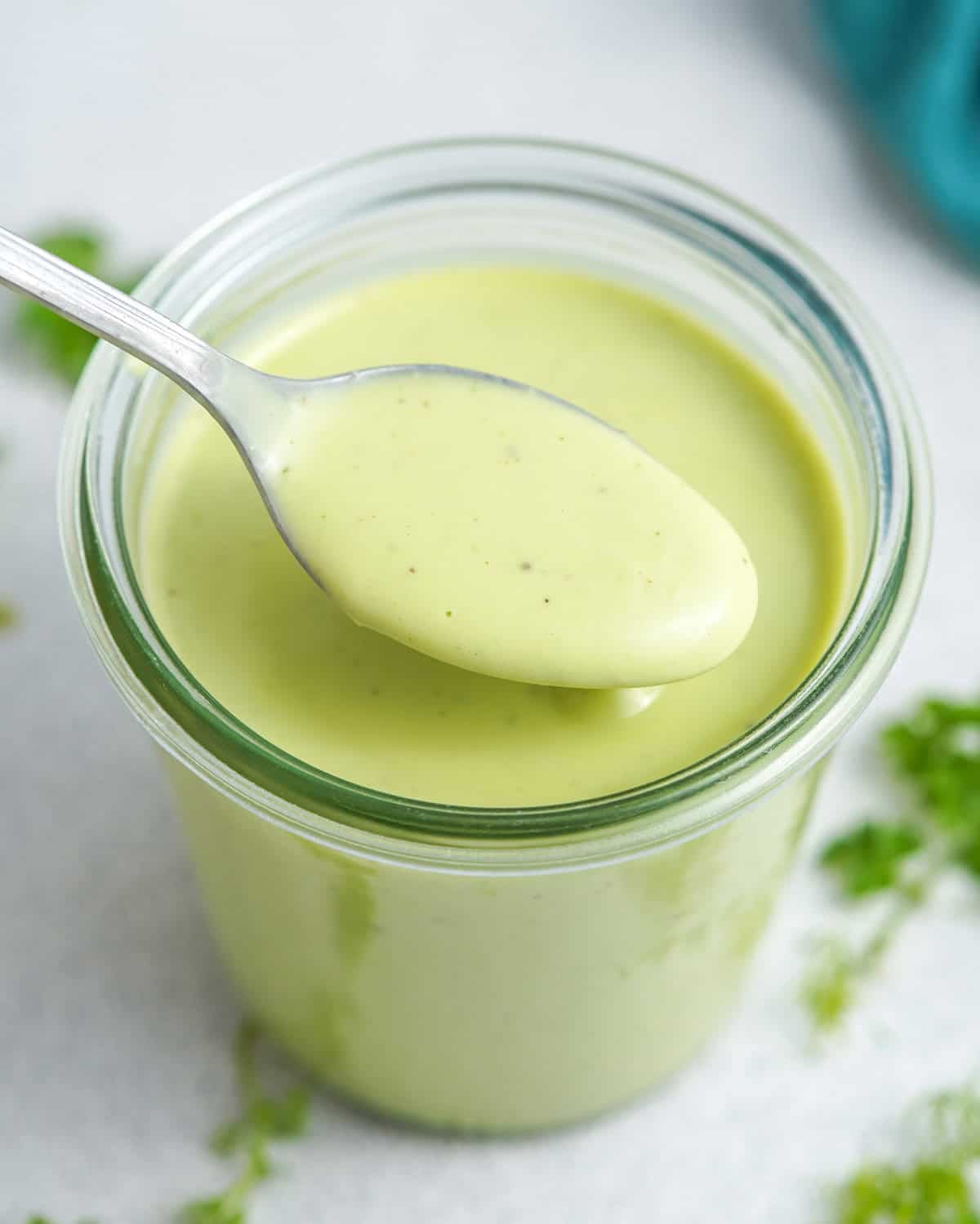 A jar of creamy avocado ranch salad dressing with a spoon scooping some out.