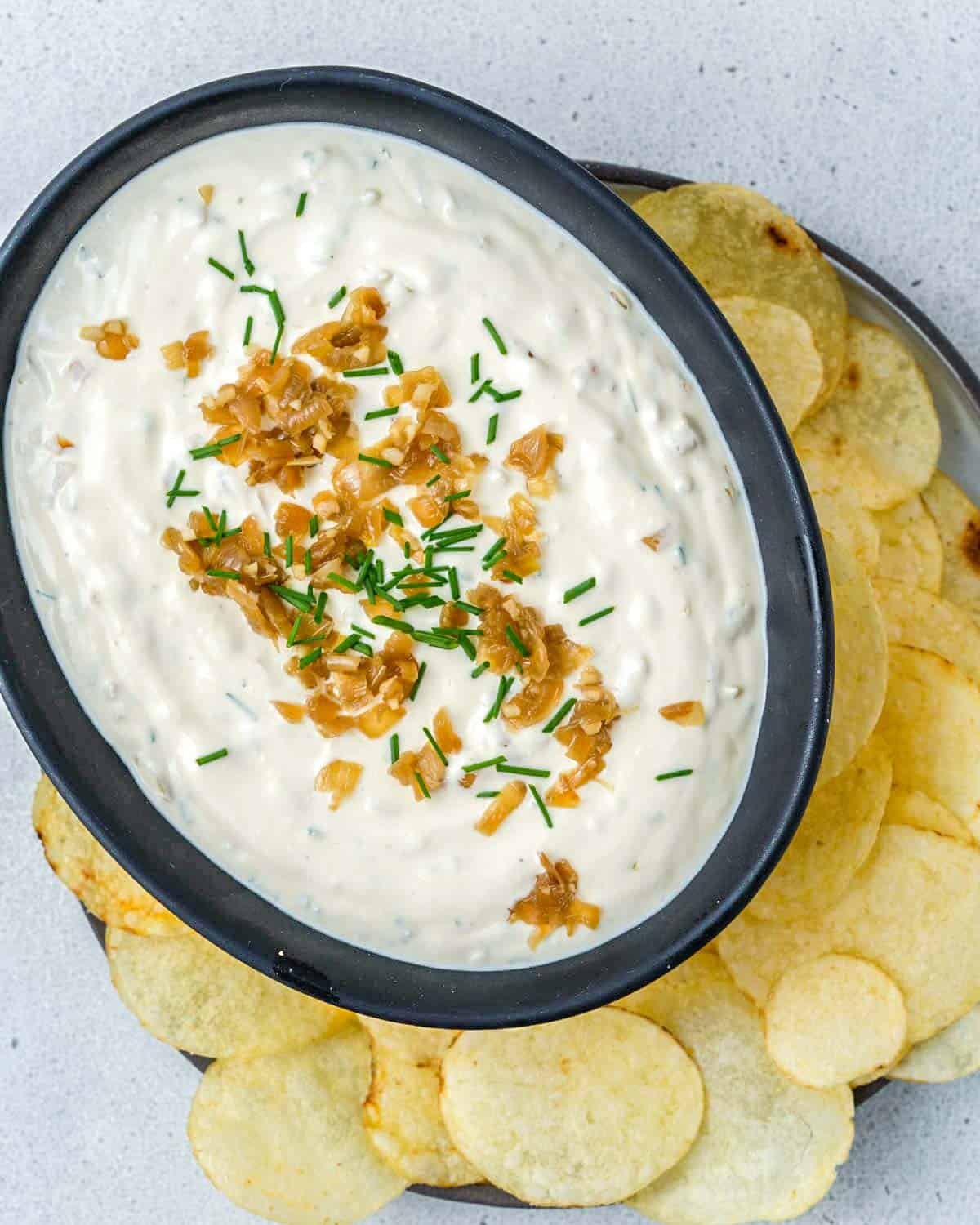 a bowl filled with french onion dip topped with chives and caramelized onions. 