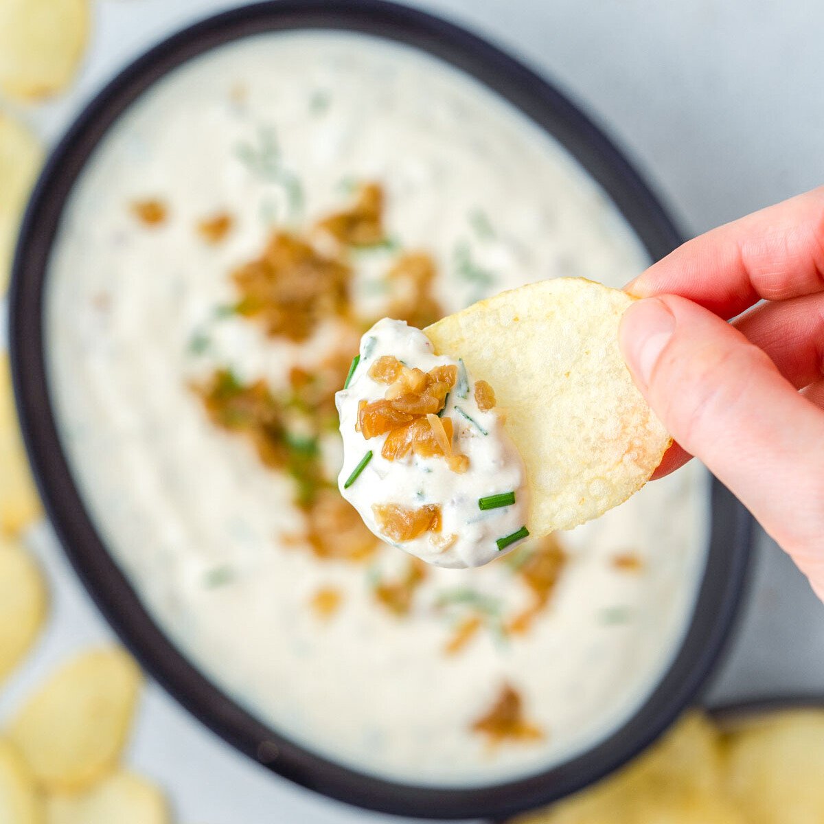 a bowl with french onion dip and grabbing a bite with chips.