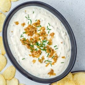 a black oval bowl with French onion dip and chips around it.