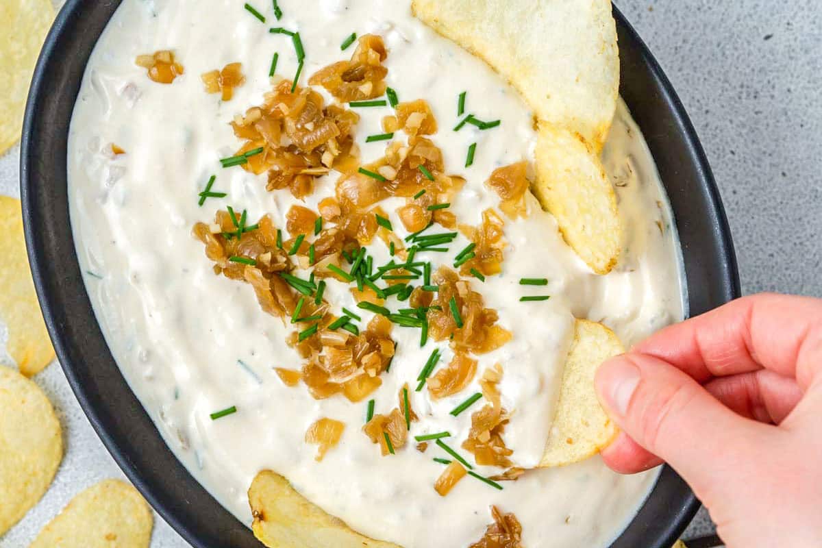 hand holding a chip and dipping in french onion dip.