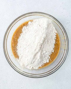 flour mixture added over the egg and banana mixture in a bowl.