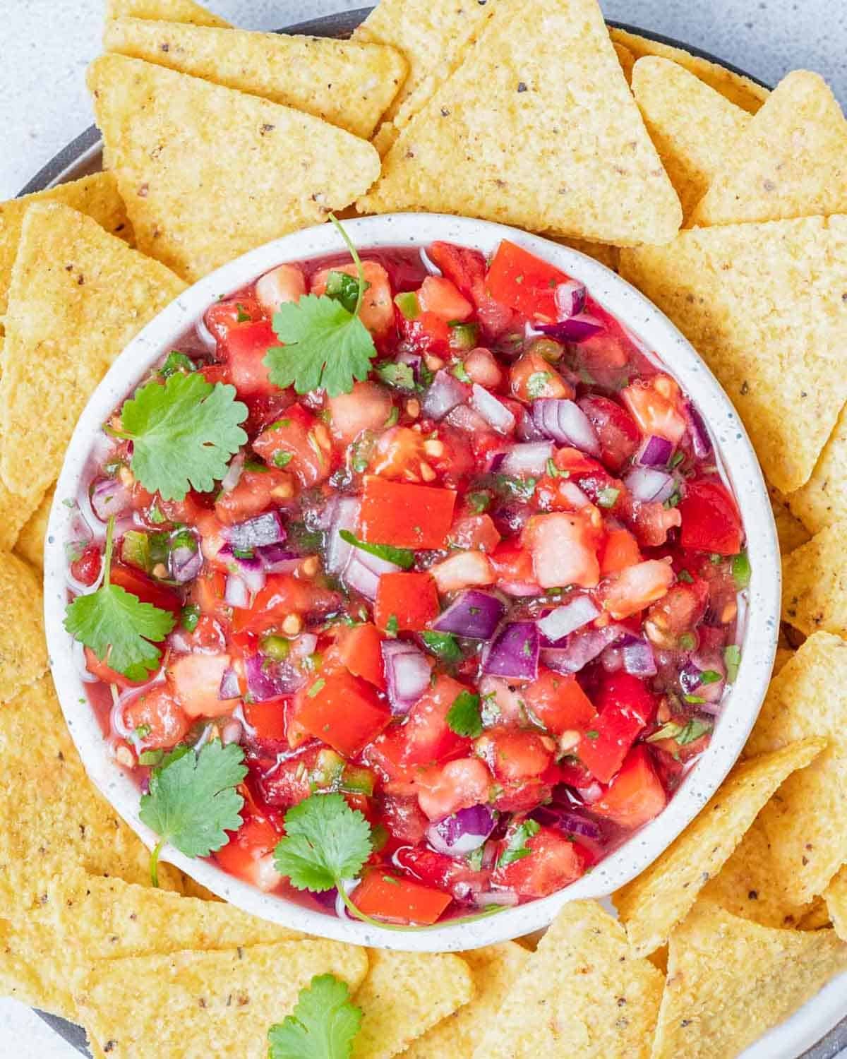 pico de gallo in a round white bowl surrounded by tortilla chips.