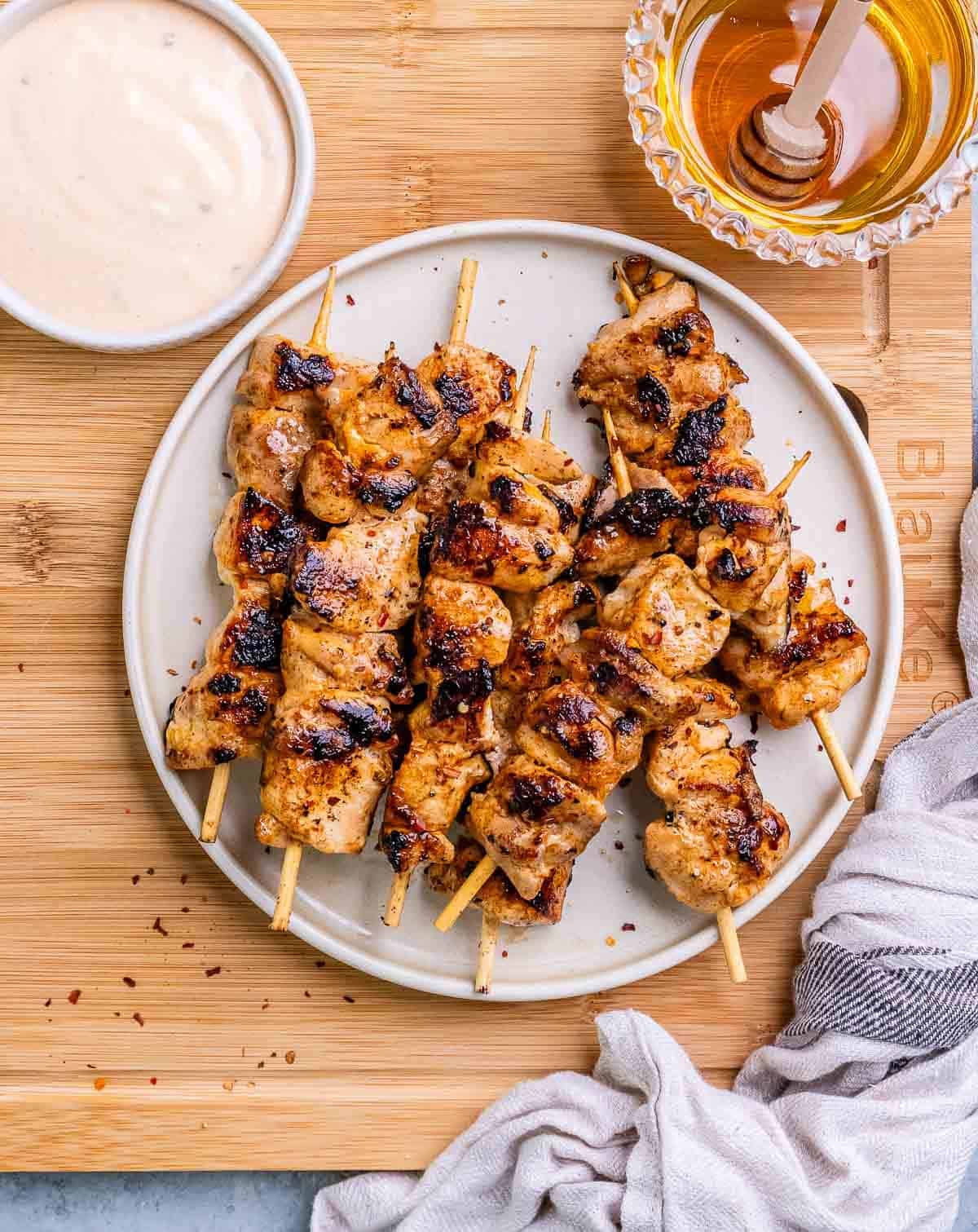 Grilled bang bang chicken skewers on a white plate on a wooden board.