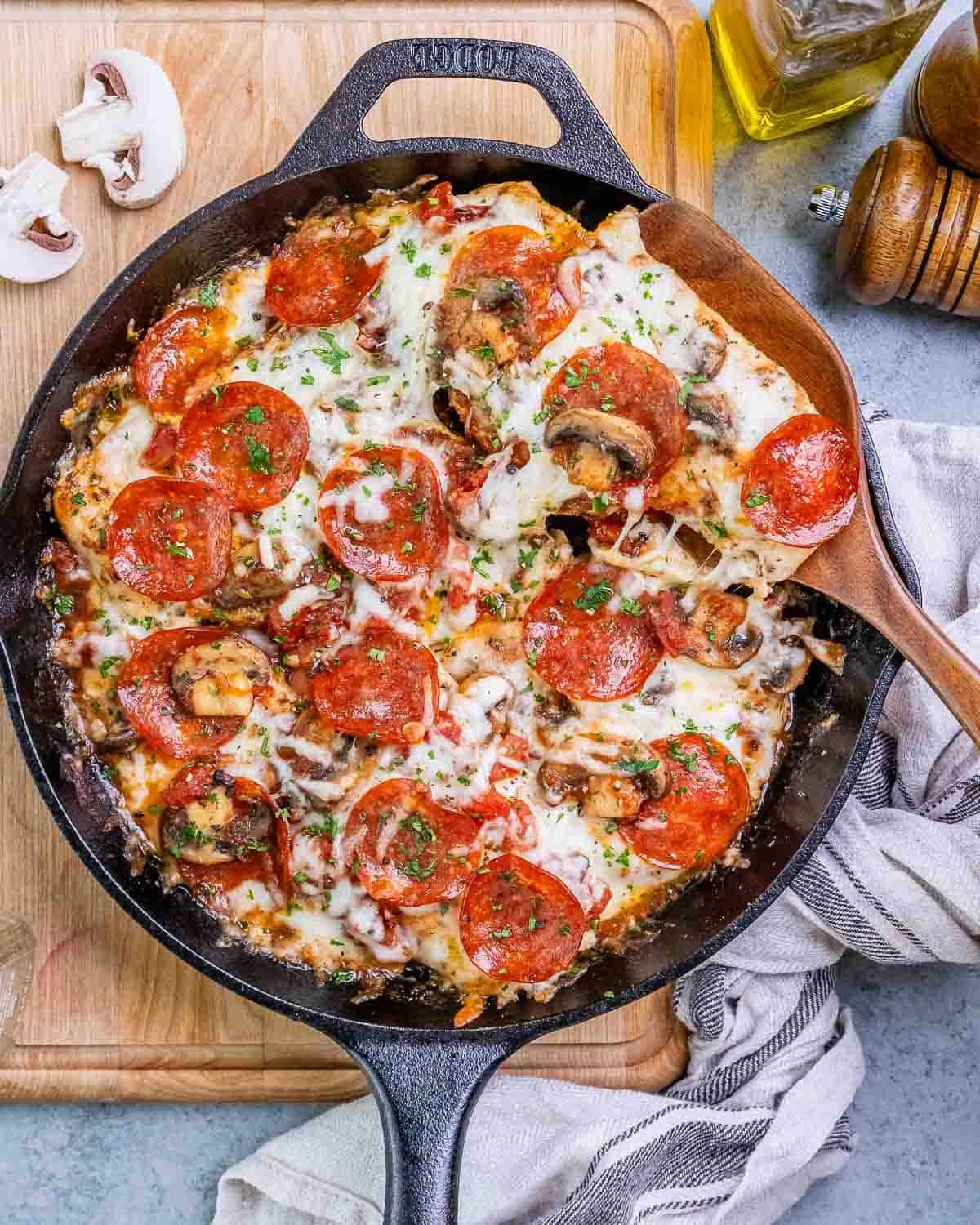 Chicken pizzaiola with mozzarella in a skillet on a wooden board.
