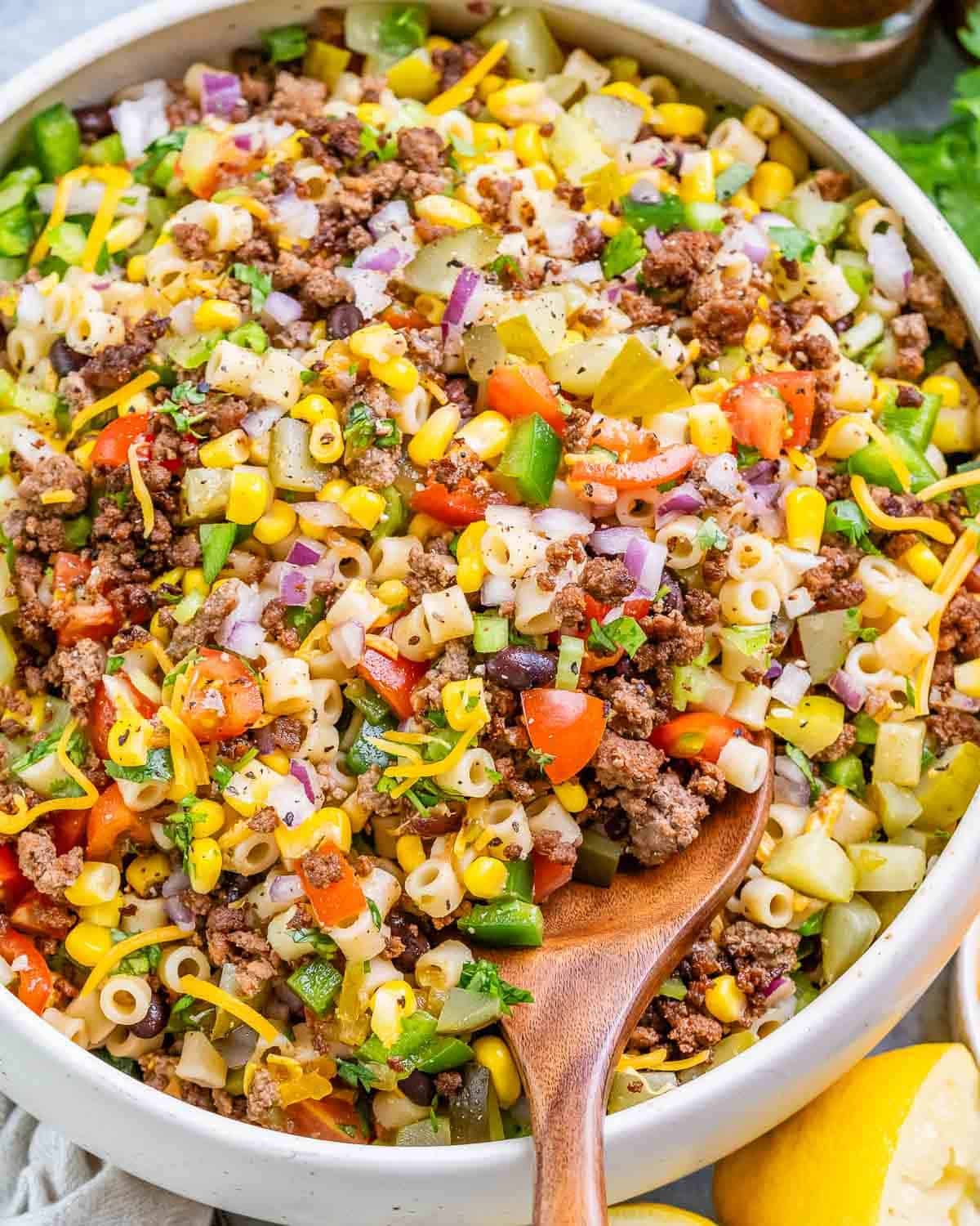 a bowl with cowboy pasta salad with a wooden spoon in the bowl.