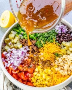 dressing poured over pasta salad with veggies and ground beef in a bowl.