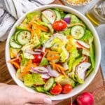 a hand holding a bowl with garden salad mixed with dressing.