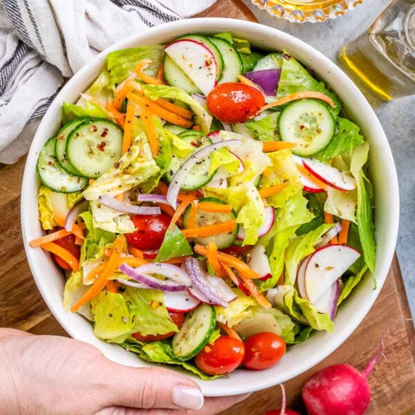 a hand holding a bowl with garden salad mixed with dressing.