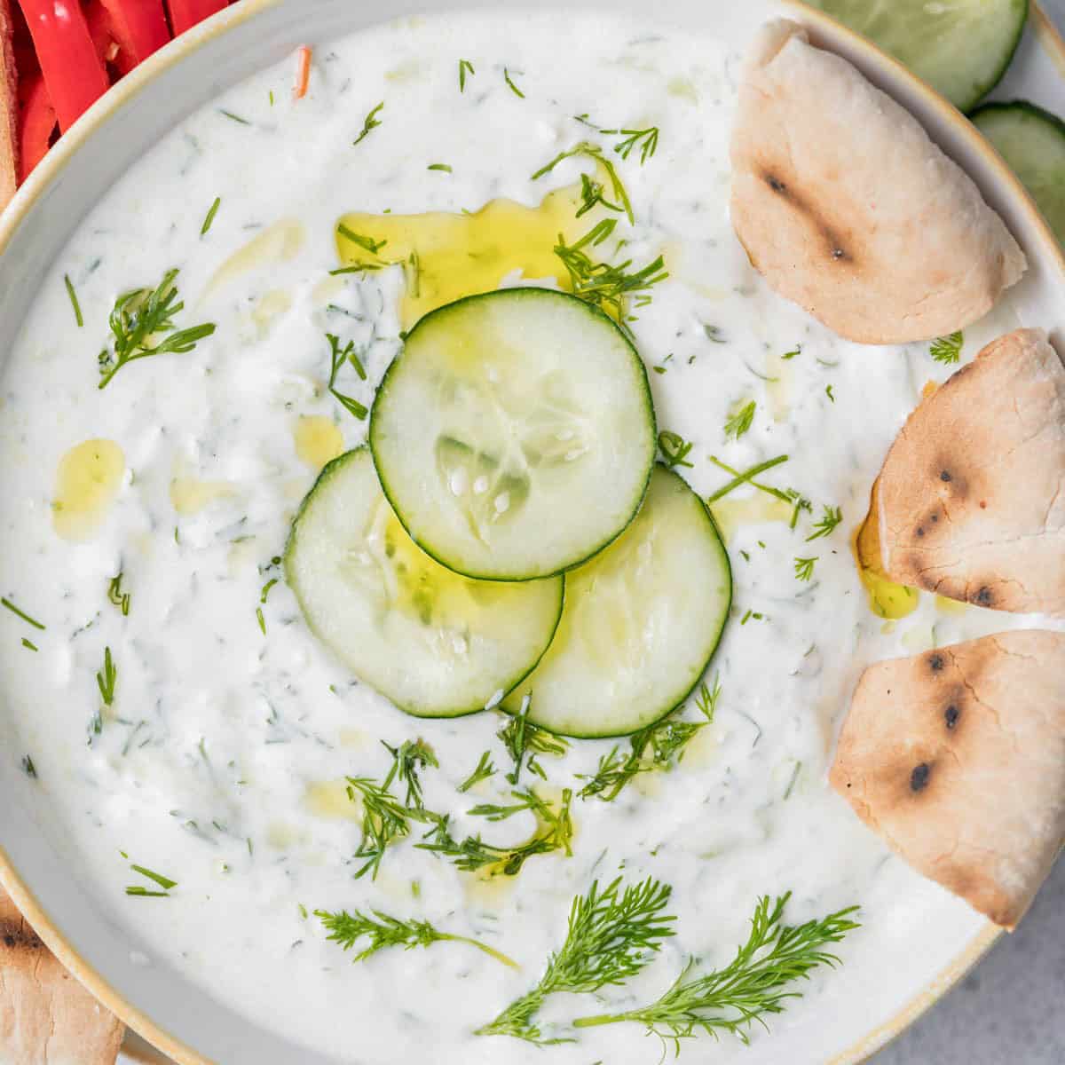 a bowl with tzatziki with 3 pieces of bread in the bowl.