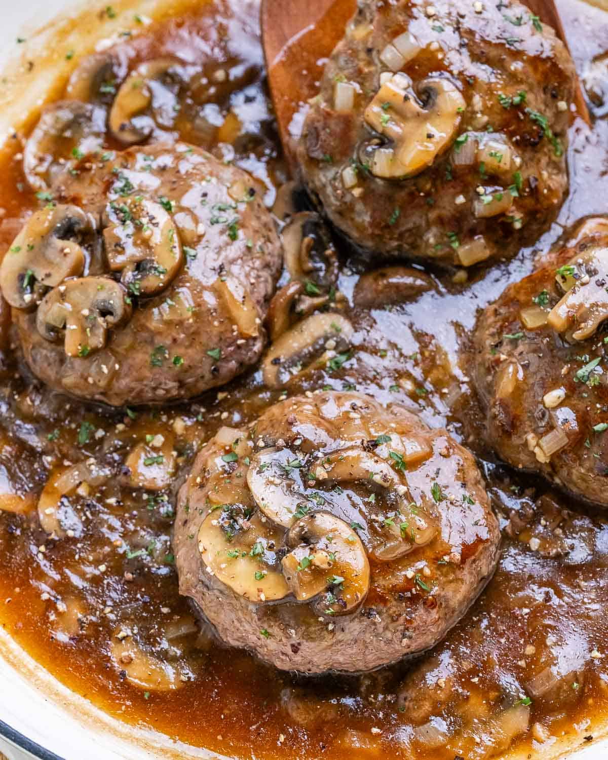 Hamburger steaks in a white skillet with mushroom onion gravy