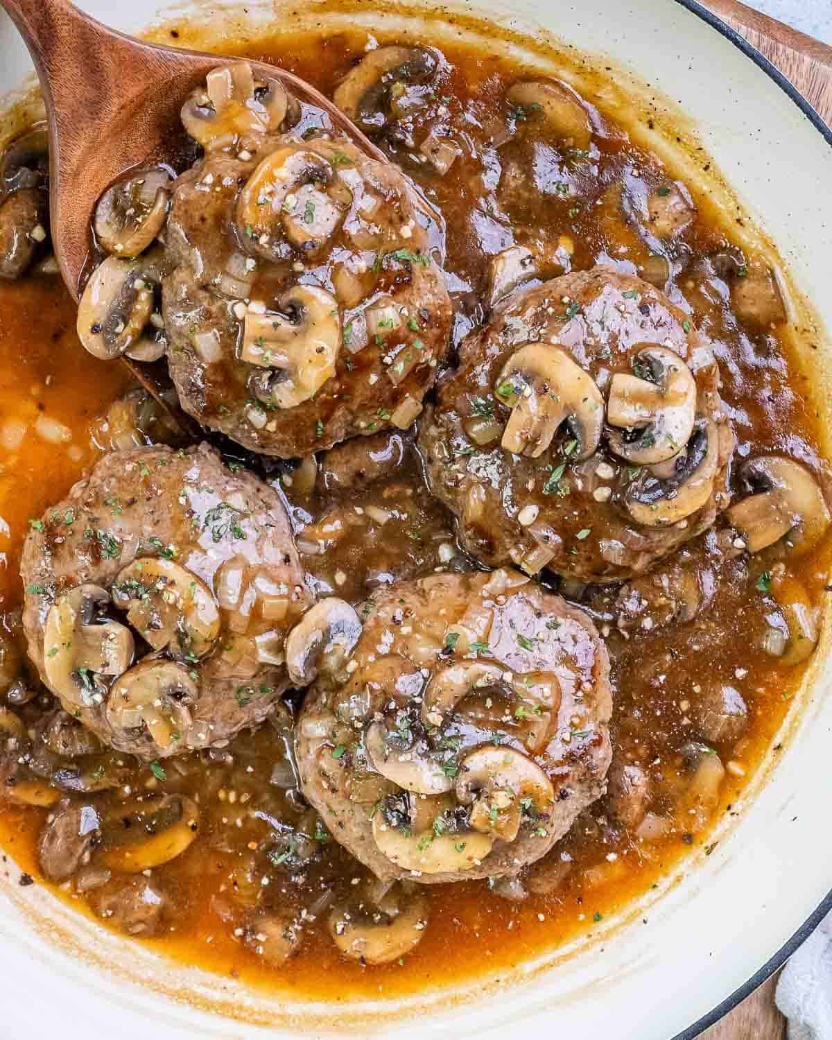 Four hamburger steaks in a white skillet with mushroom gravy.