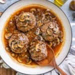 4 hamburger steaks in a skillet with mushroom sauce.