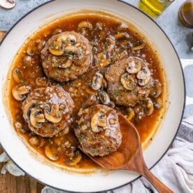 4 hamburger steaks in a skillet with mushroom sauce.