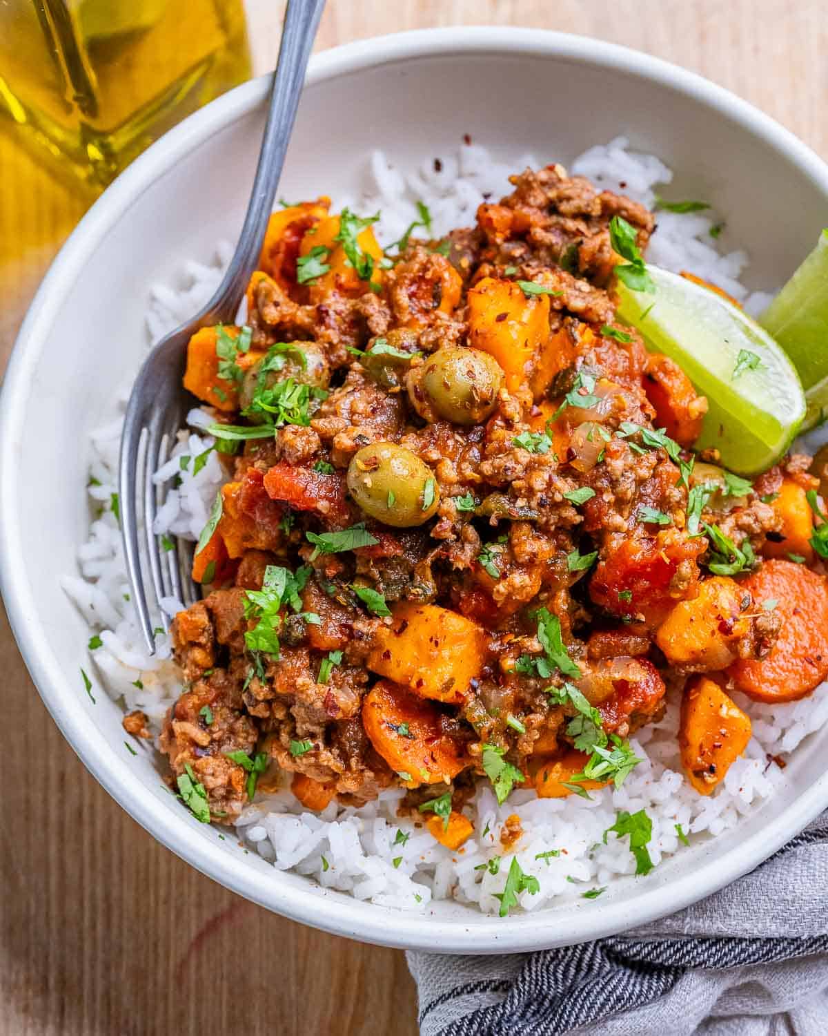 A white bowl of rice with Mexican picadillo and lime wedges.