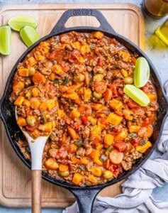 A black skillet of Mexican picadillo on a wooden board.