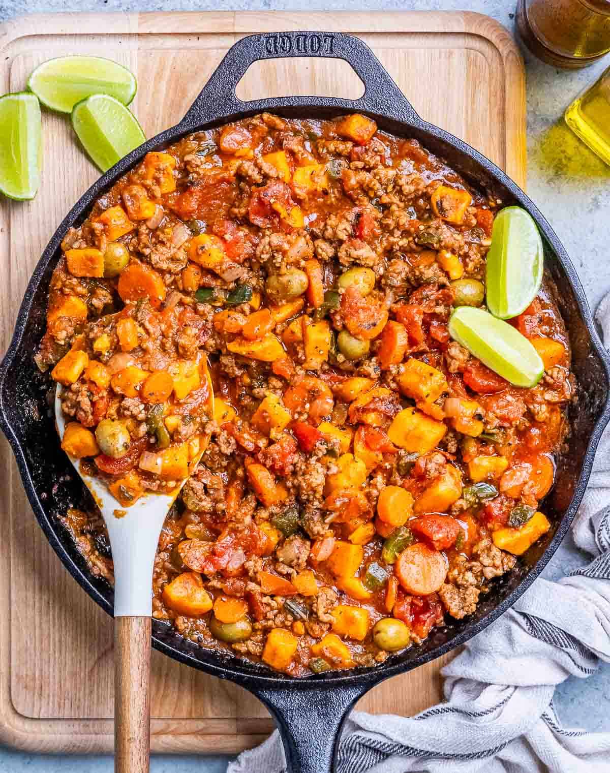 A black skillet of Mexican picadillo on a wooden board.