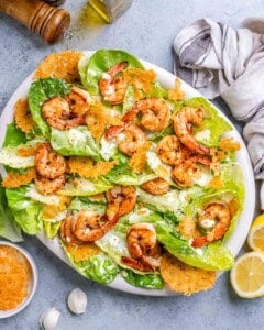 Shrimp caesar salad on a white oval plate with parmesan crisps.