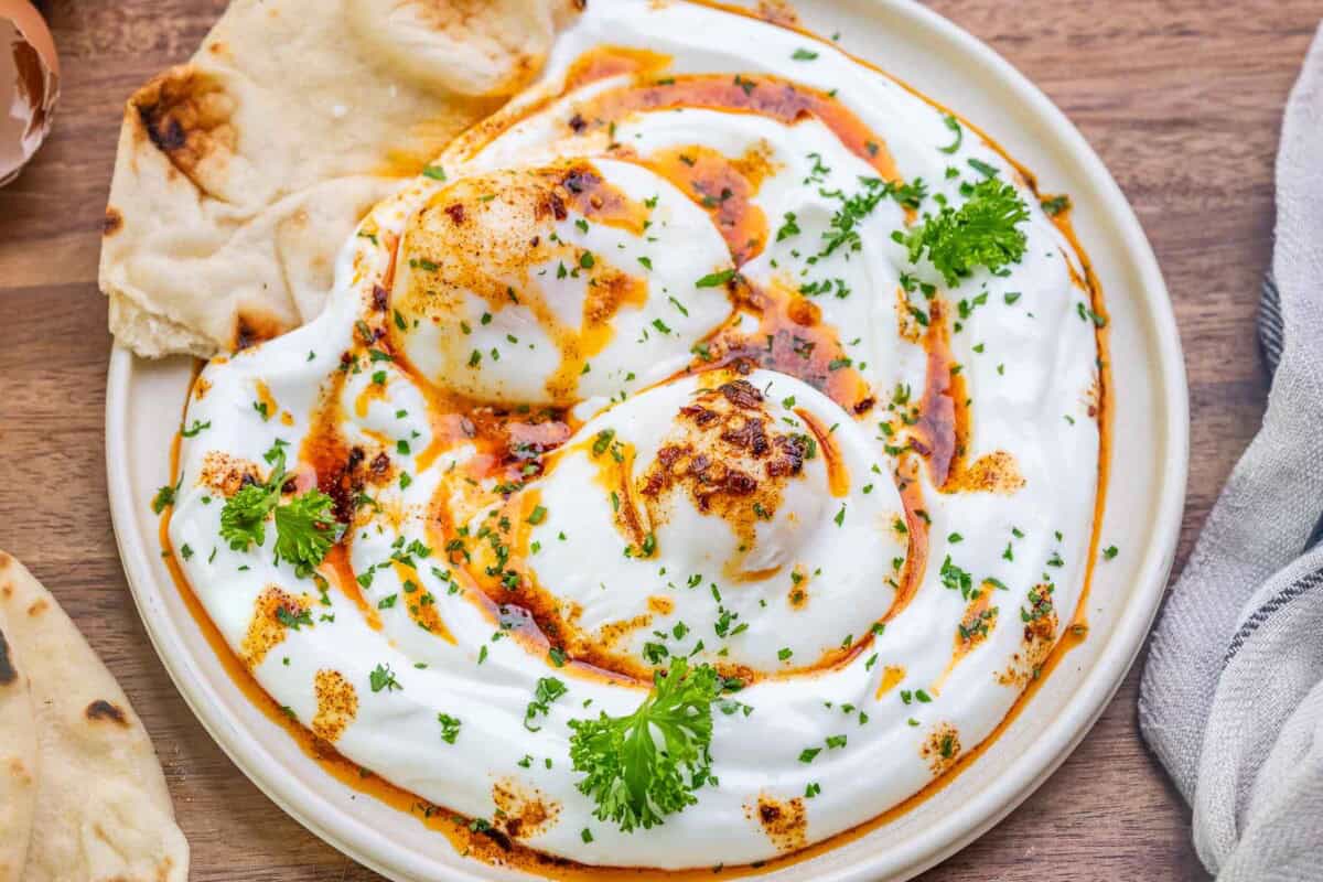 a bowl with turkish eggs over a bed of garlic yogurt with a side of naan bread.