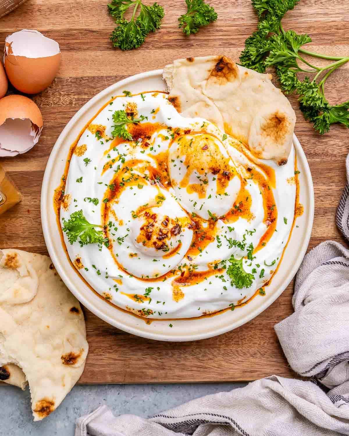 A white bowl of Turkish eggs on a wooden board.