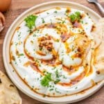 Turkish eggs over garlic yogurt on a plate thats drizzled with chili oil.