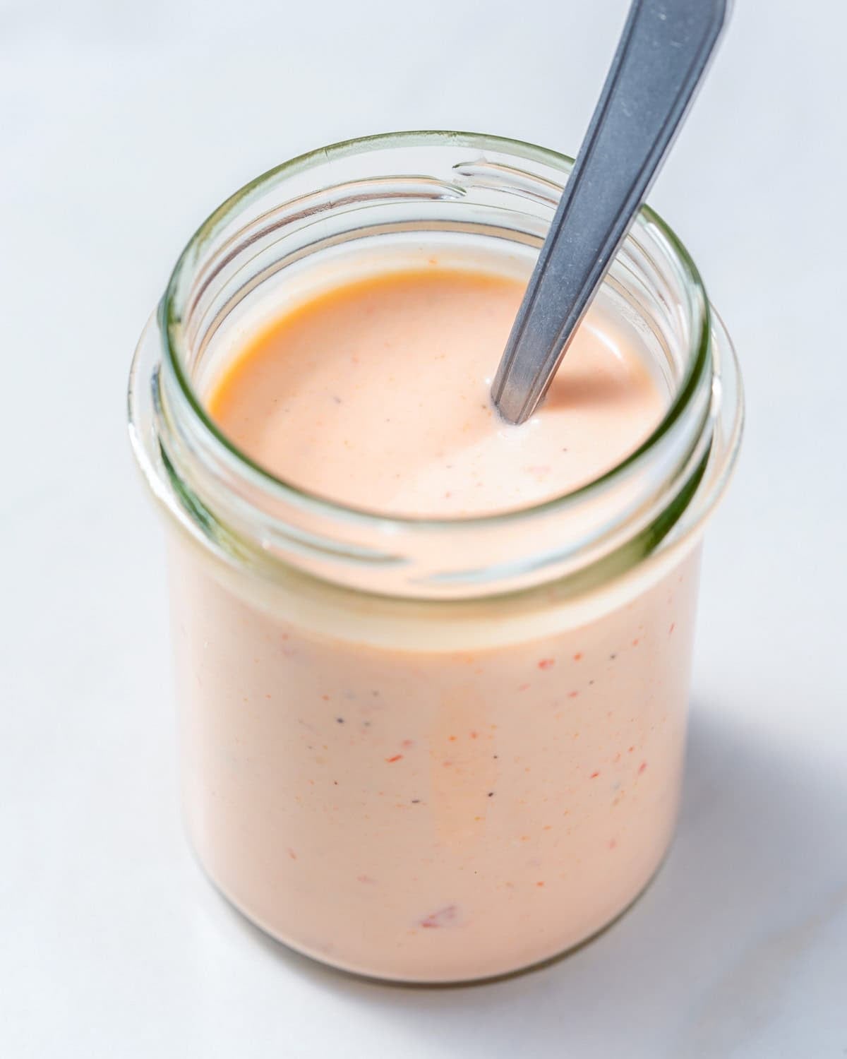 A jar with bang bang sauce with a spoon in the jar.