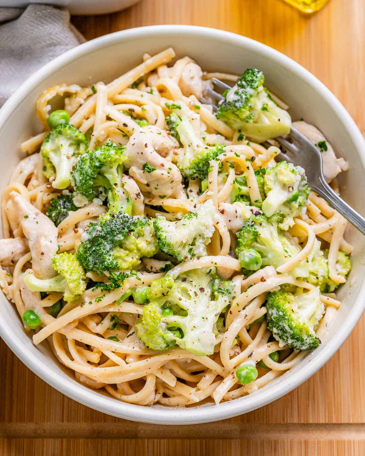A white bowl of chicken tetrazzini with broccoli and peas.