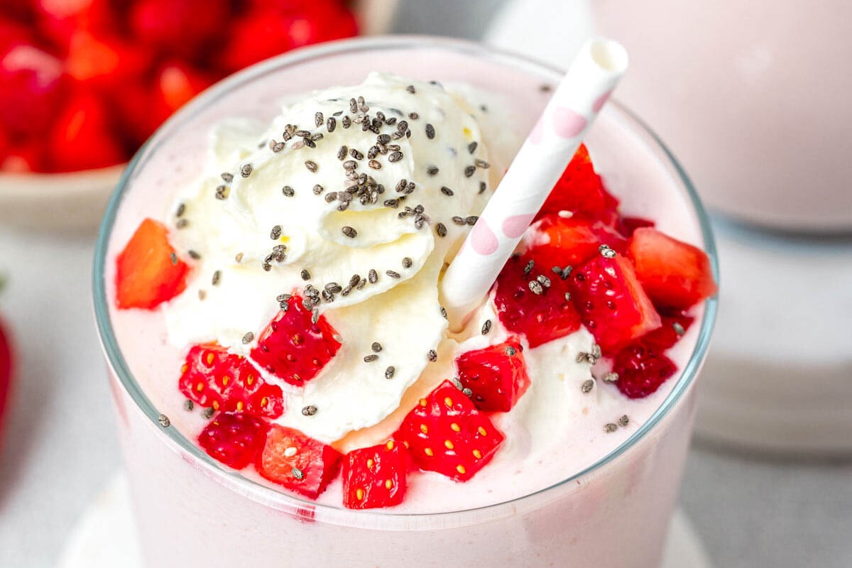 a cup with strawberry smoothie topped with whipped cream, diced fresh strawberries, and chia seeds.