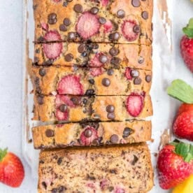 sliced banana bread made with chocolate chips and fresh strawberries on a cutting board.