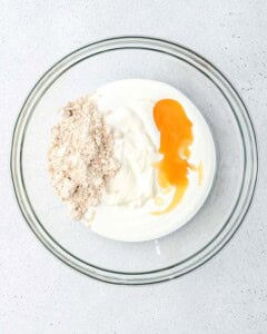 Clear glass bowl with vanilla Greek yogurt, a scoop of vanilla whey protein powder, and a drizzle of honey added on top.