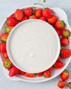 Large white serving bowl surrounded by a ring of fresh whole strawberries on a white plate.