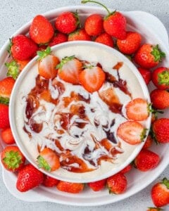 a bowl with strawberry fruit dip surrounded by fresh strawberries.
